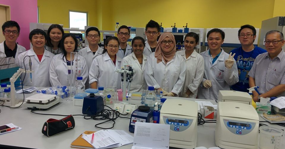 A group of participants and trainers in lab coats standing behind a laboratory bench