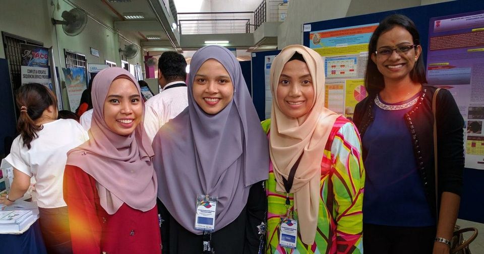 Four smiling delegates stand together in front of research posters