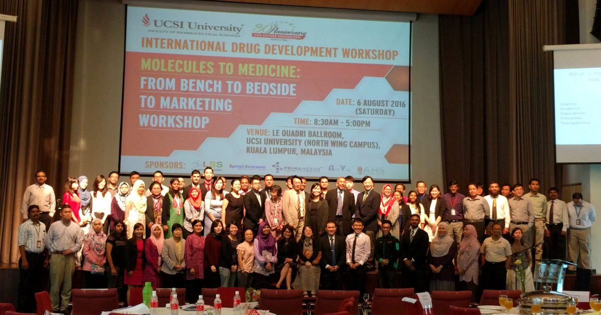 Large group of workshop participants on stage in front of a screen showing the workshop title and sponsors