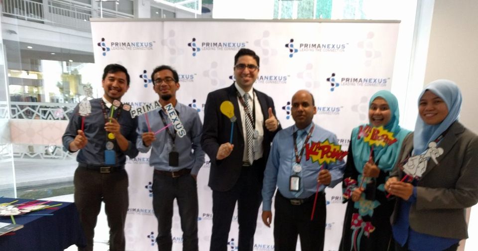 Six participants holding photo props in front of the Prima Nexus backdrop