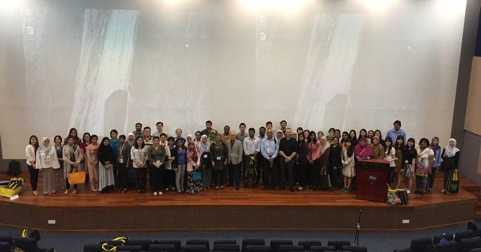 Course participants standing together on the auditorium stage for a group photo, rows of empty seats in front