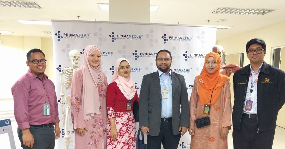 Six delegates and organisers stand in front of the Prima Nexus photo wall, beside an anatomical skeleton model
