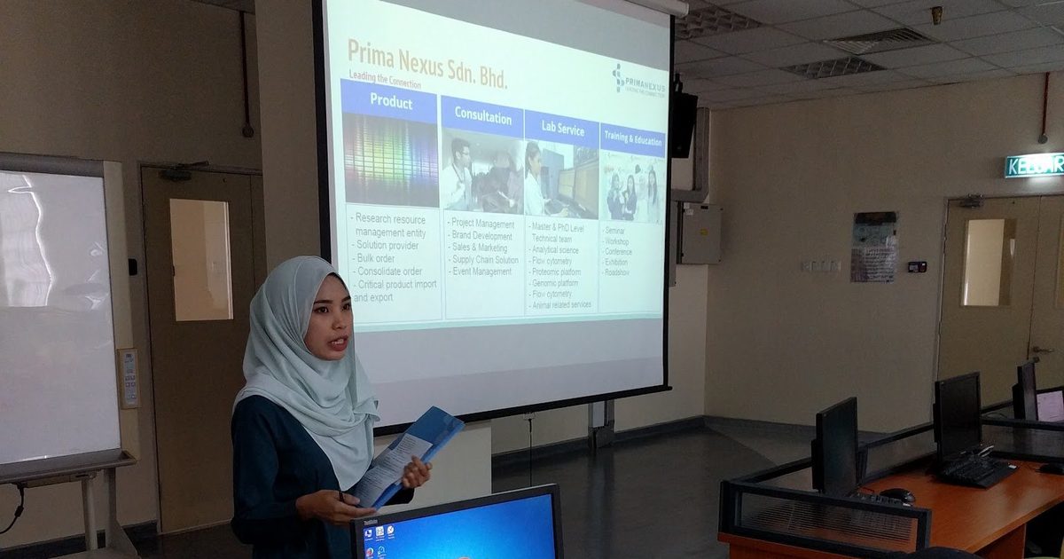 A presenter beside the screen while participants work at computers in the computer laboratory