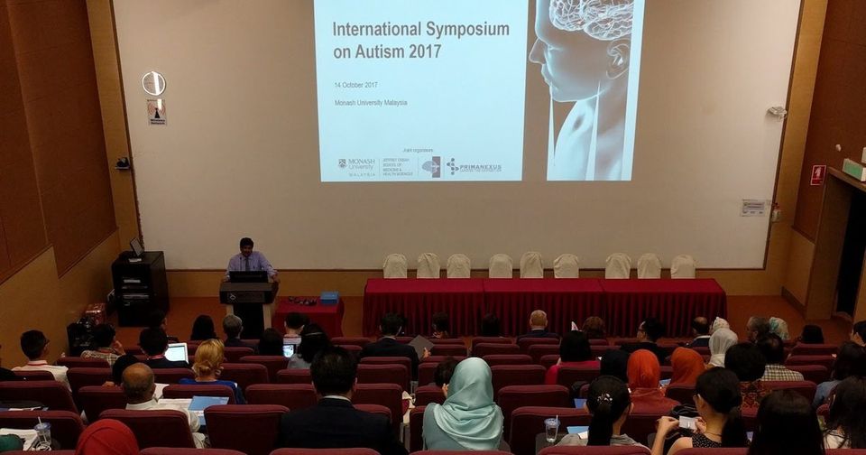 The Plenary Theatre at Monash University Malaysia, with the symposium title on the screen and the audience seated