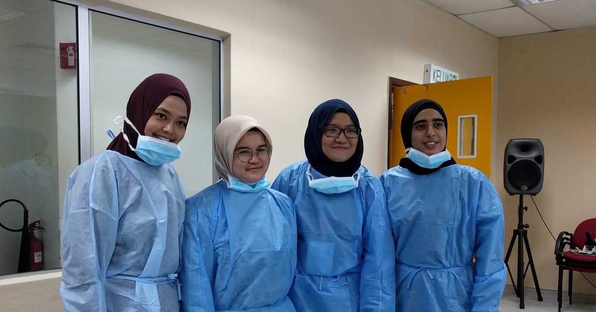 Four participants in blue gowns stand together for a photo in the workshop room