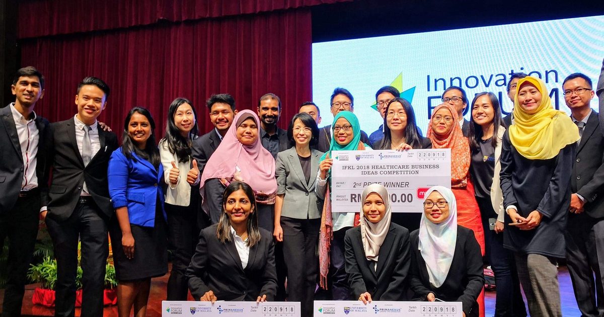 Winners of the IFKL 2018 business ideas competition kneel with large prize cheques in front of organisers and guests, below the Innovation Forum screen