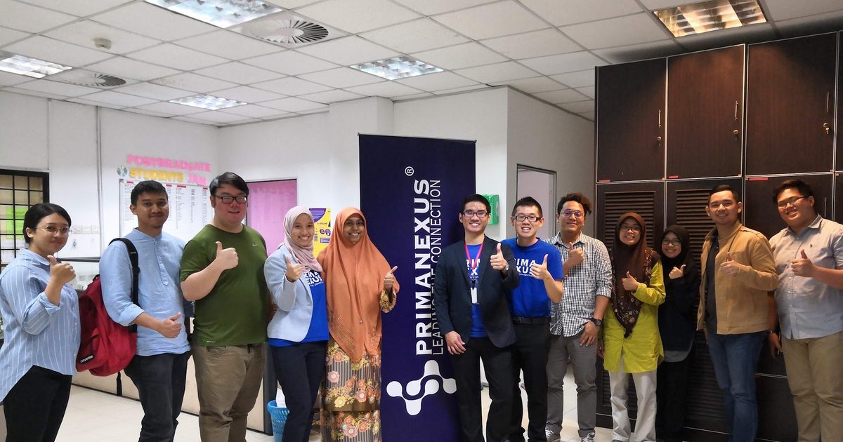 Workshop participants and trainers stand in a row for a group photo beside a Prima Nexus banner