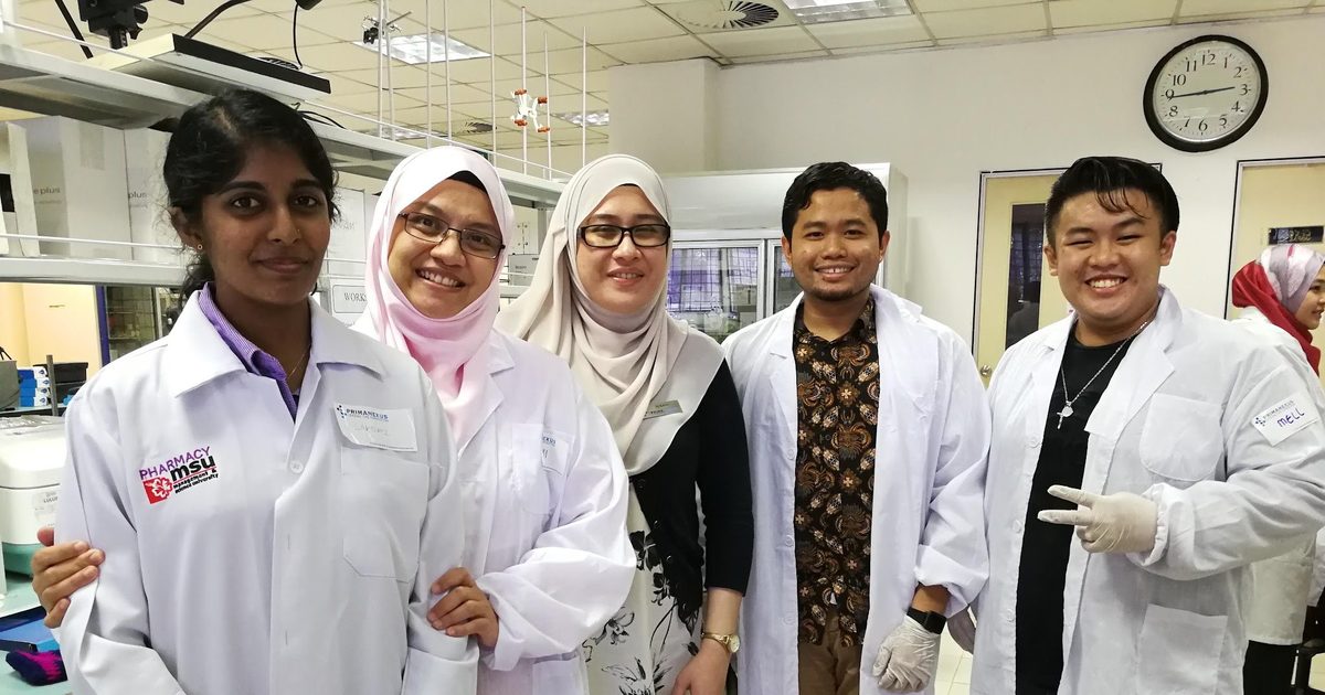 Participants and trainers in lab coats stand together for a group photo in the laboratory