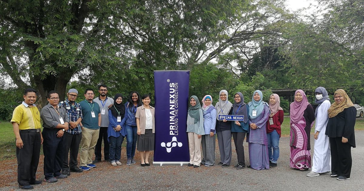 Workshop participants and speakers in a group photo outdoors, beside a Prima Nexus banner