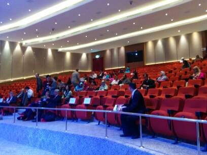 Delegates seated in the red-seat auditorium at Connexion@Nexus, seen from the side aisle