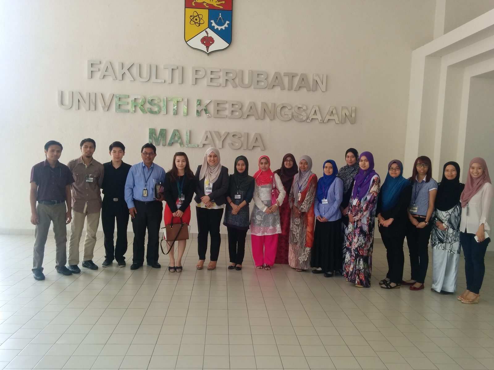 A group of about twenty people standing in a row under the Faculty of Medicine, UKM wall sign