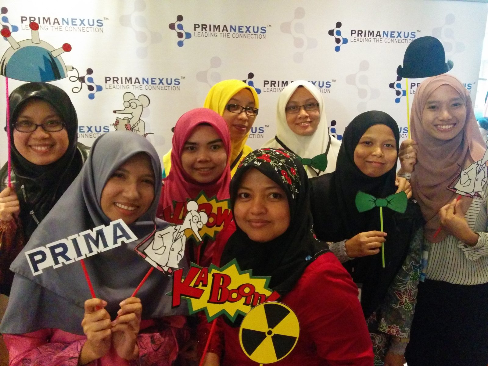 A group of delegates smiling and holding props in front of the Prima Nexus photo wall
