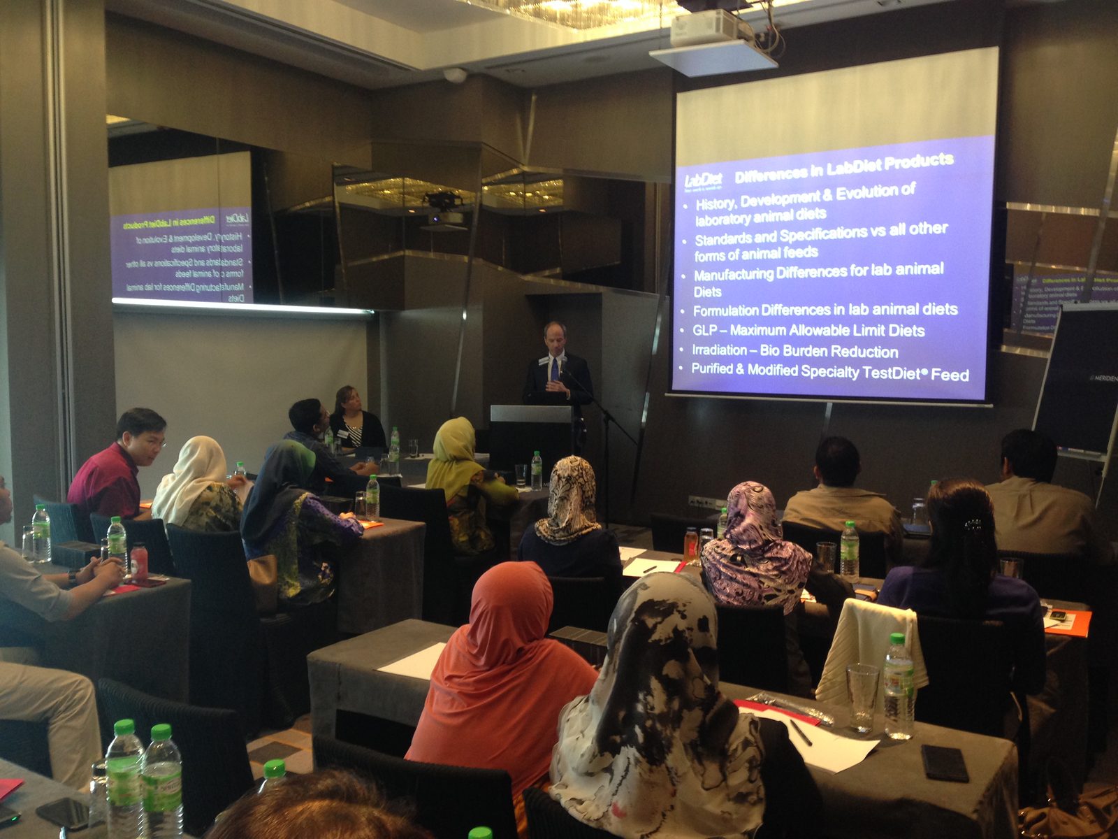 A speaker at the lectern presents a slide on differences in LabDiet products to a seated audience