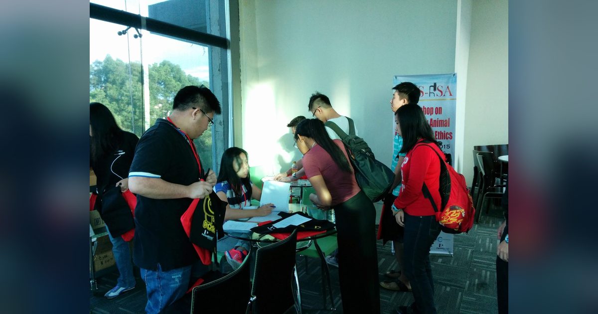 Participants sign in at the registration table, holding red workshop bags, with the workshop banner standing behind them