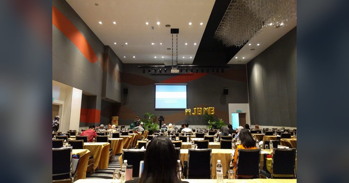Delegates seated at long tables in the conference hall, facing a screen and a stage with MSBMB balloon letters