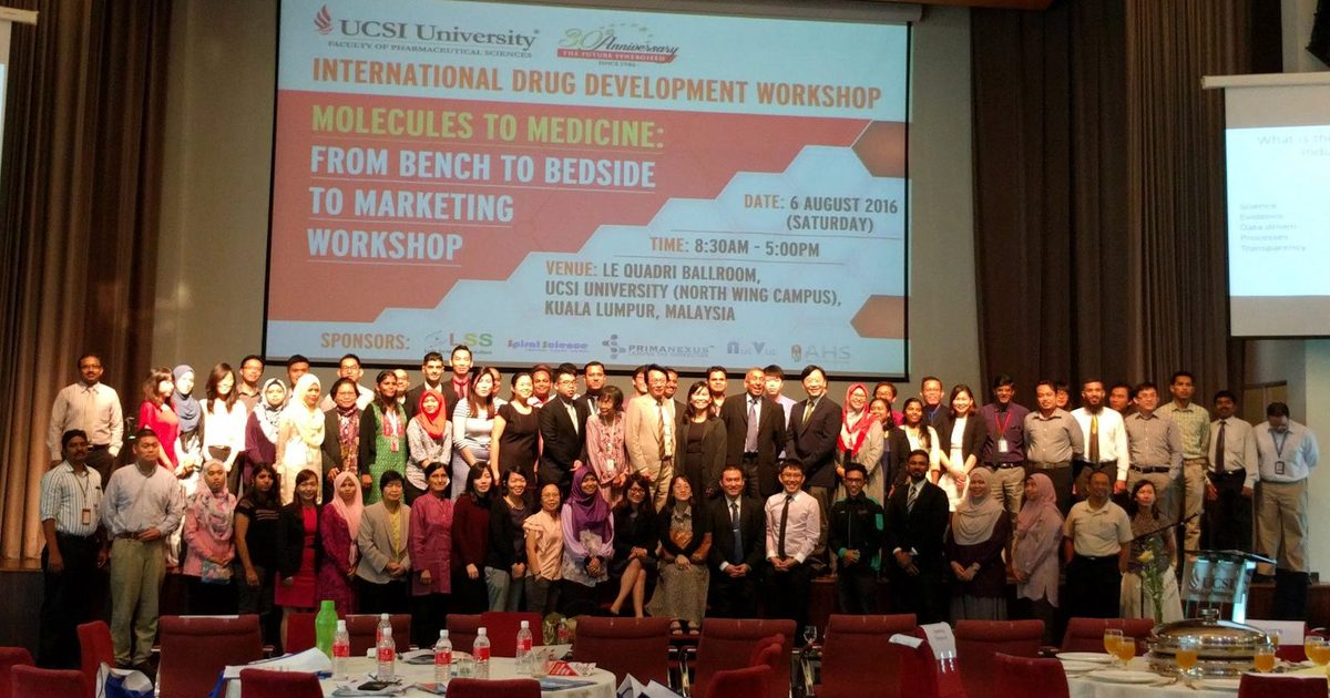 Large group of workshop participants on stage in front of a screen showing the workshop title and sponsors