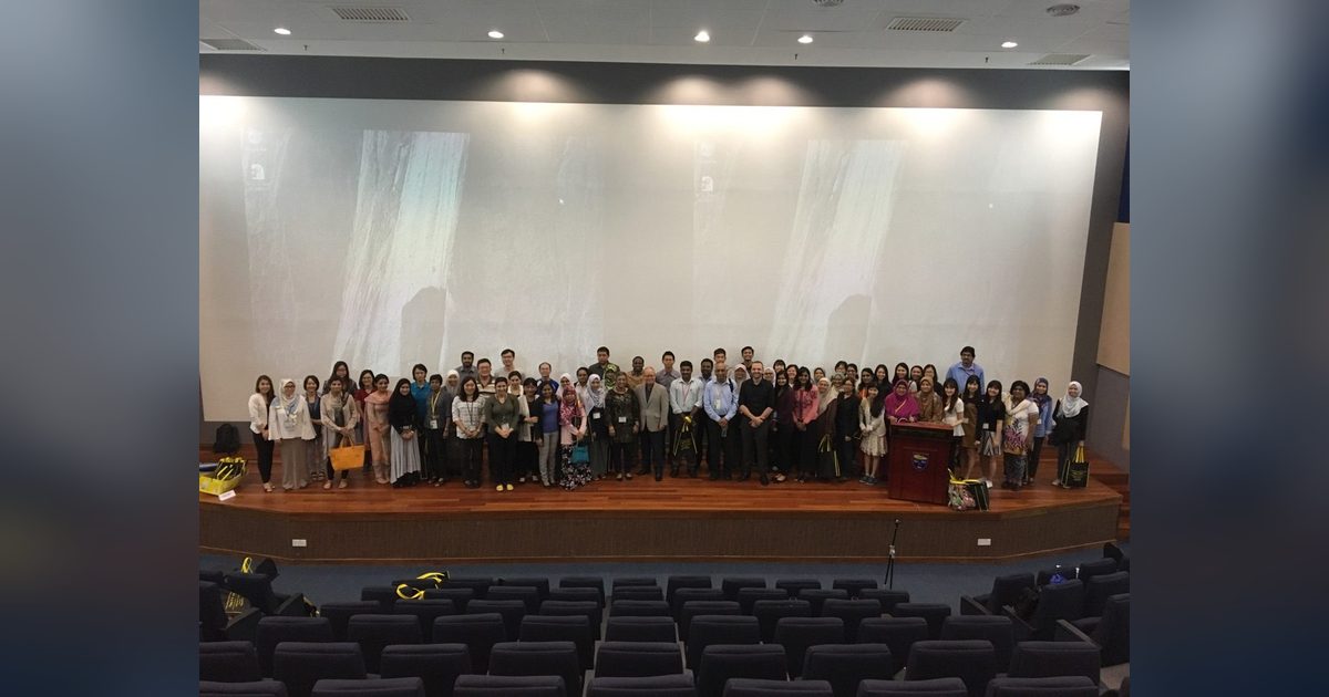 Course participants standing together on the auditorium stage for a group photo, rows of empty seats in front