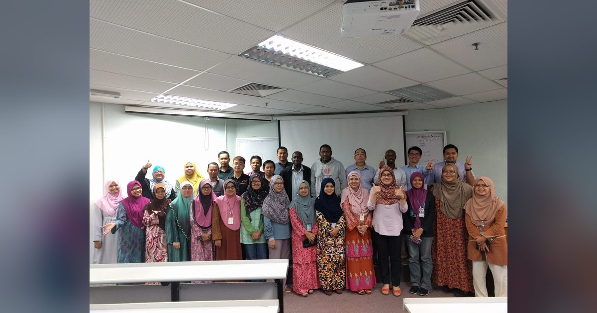 Group photo of the workshop participants standing in rows in front of the screen in a lecture room