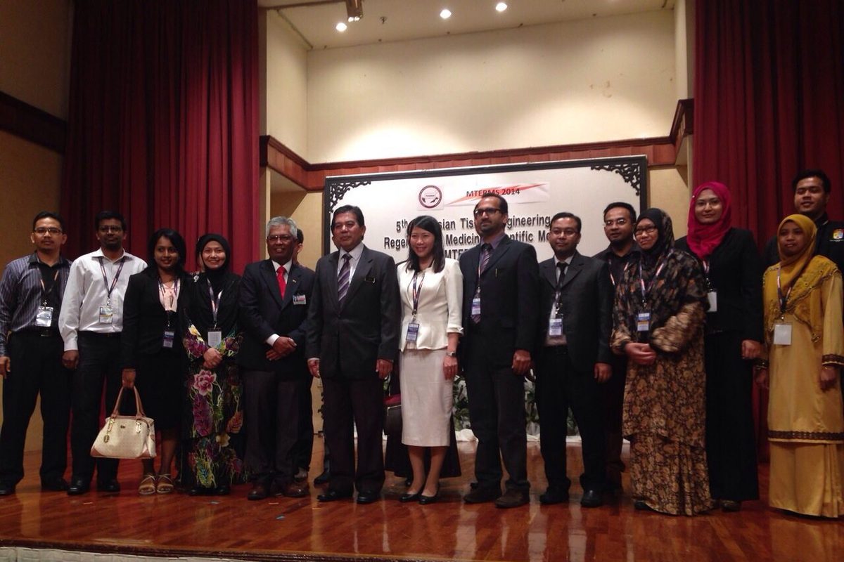 Delegates and guests stand in a row on the stage, in front of a board with the meeting name