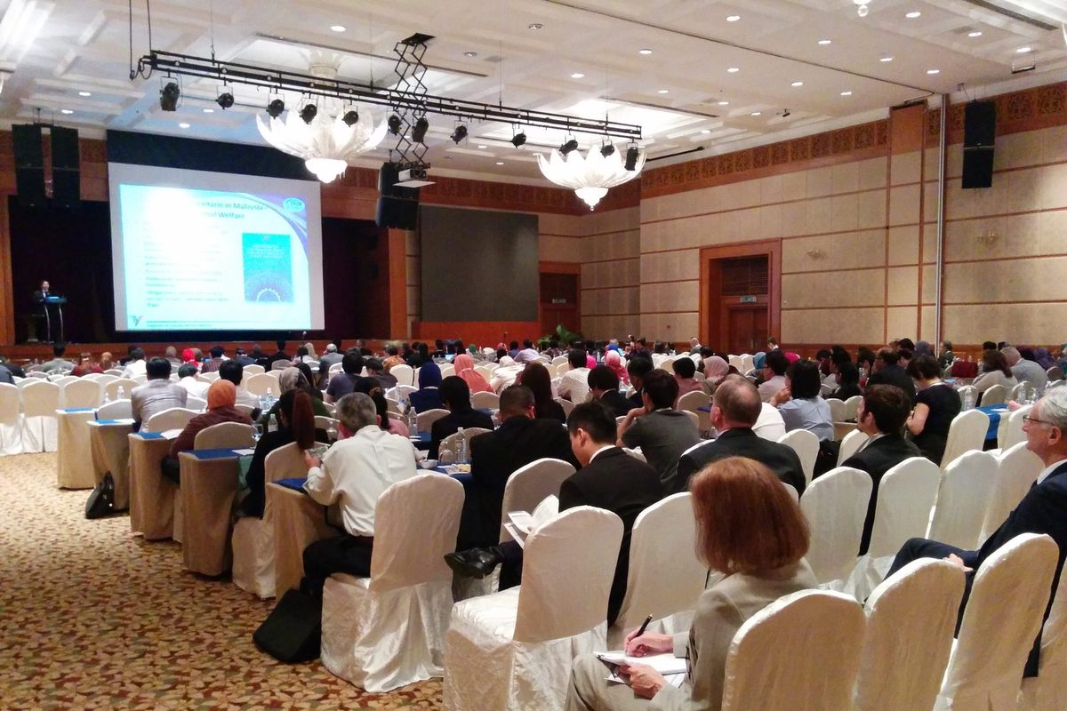 Delegates seated in rows in a large ballroom, facing a speaker and a slide on animal welfare in Malaysia