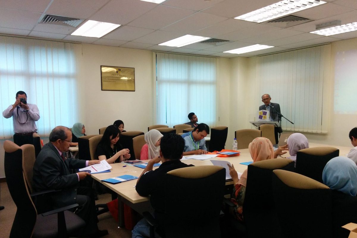 Participants at long tables in the seminar room while a photographer stands at the side