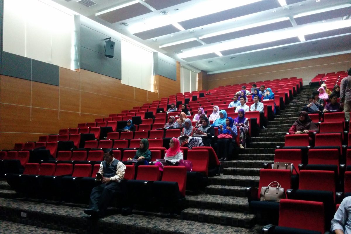 Participants seated in a tiered lecture theatre with red seats
