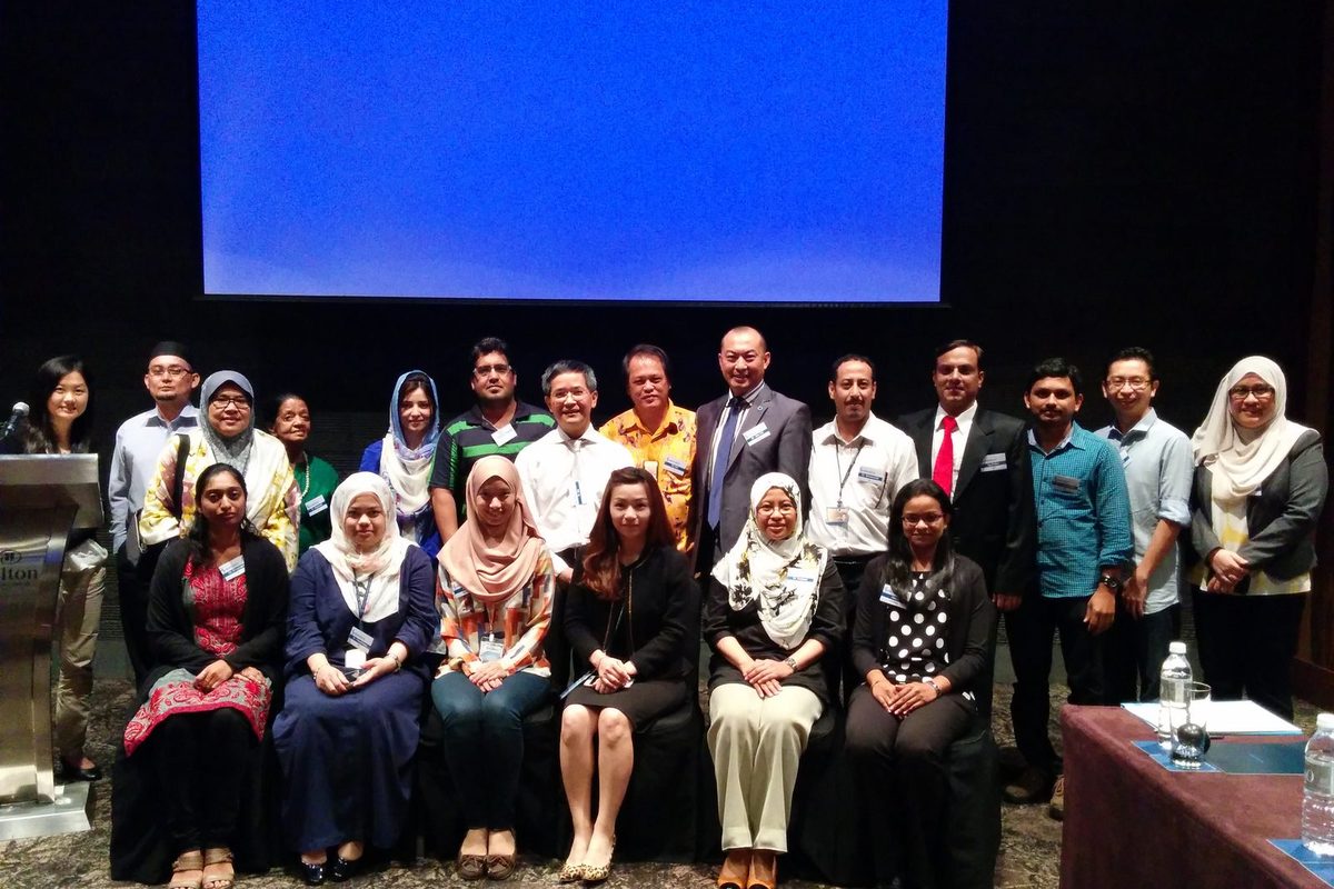 Group photo of participants standing and seated in front of the screen at Hilton Hotel, KL Sentral