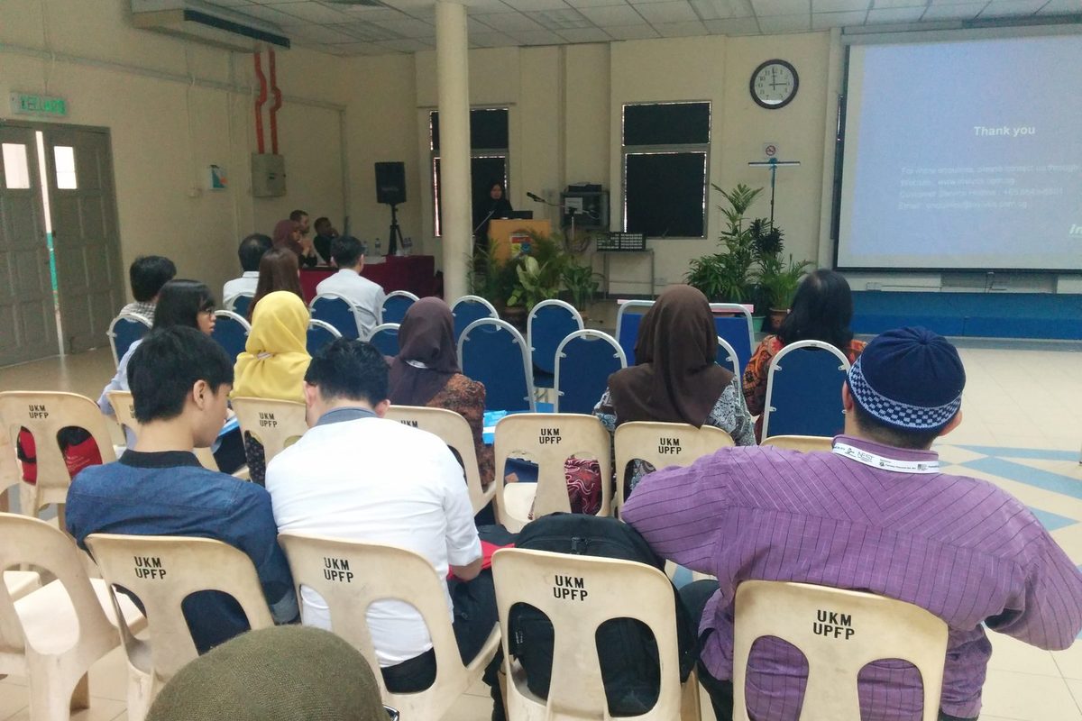 Participants seated in rows facing a speaker at the lectern and a projection screen in a hall