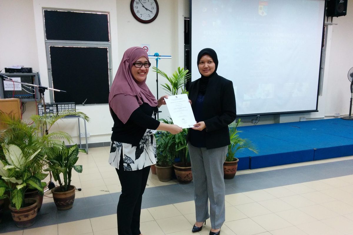 Two women holding a certificate together in front of a projection screen and potted plants