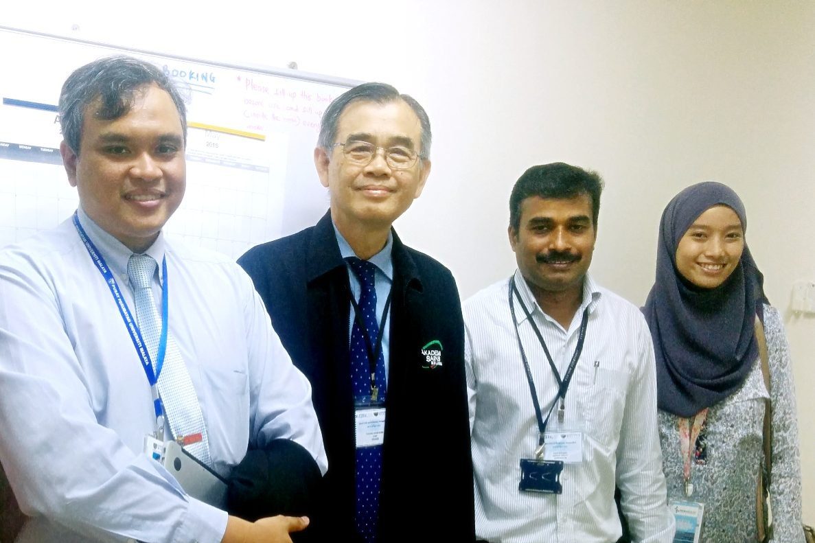 Four people stand together for a photo in a corridor
