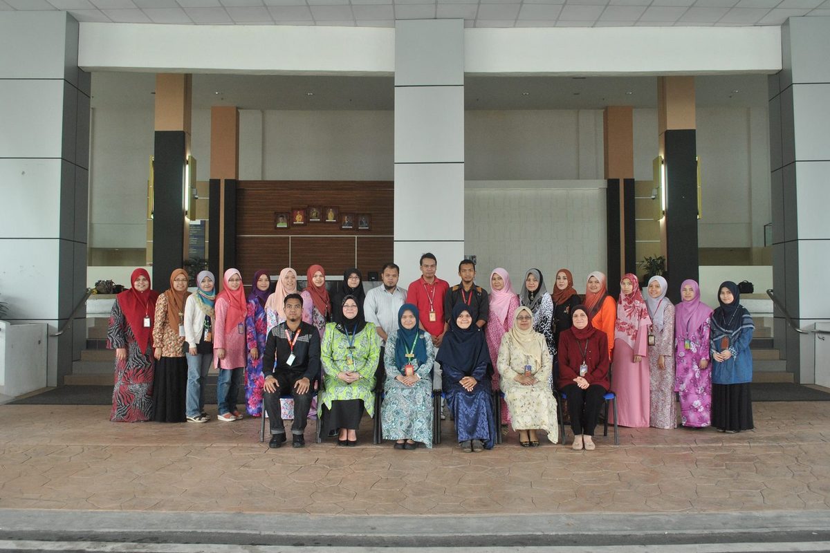 Participants standing and seated in two rows for a group photo in front of a campus building.