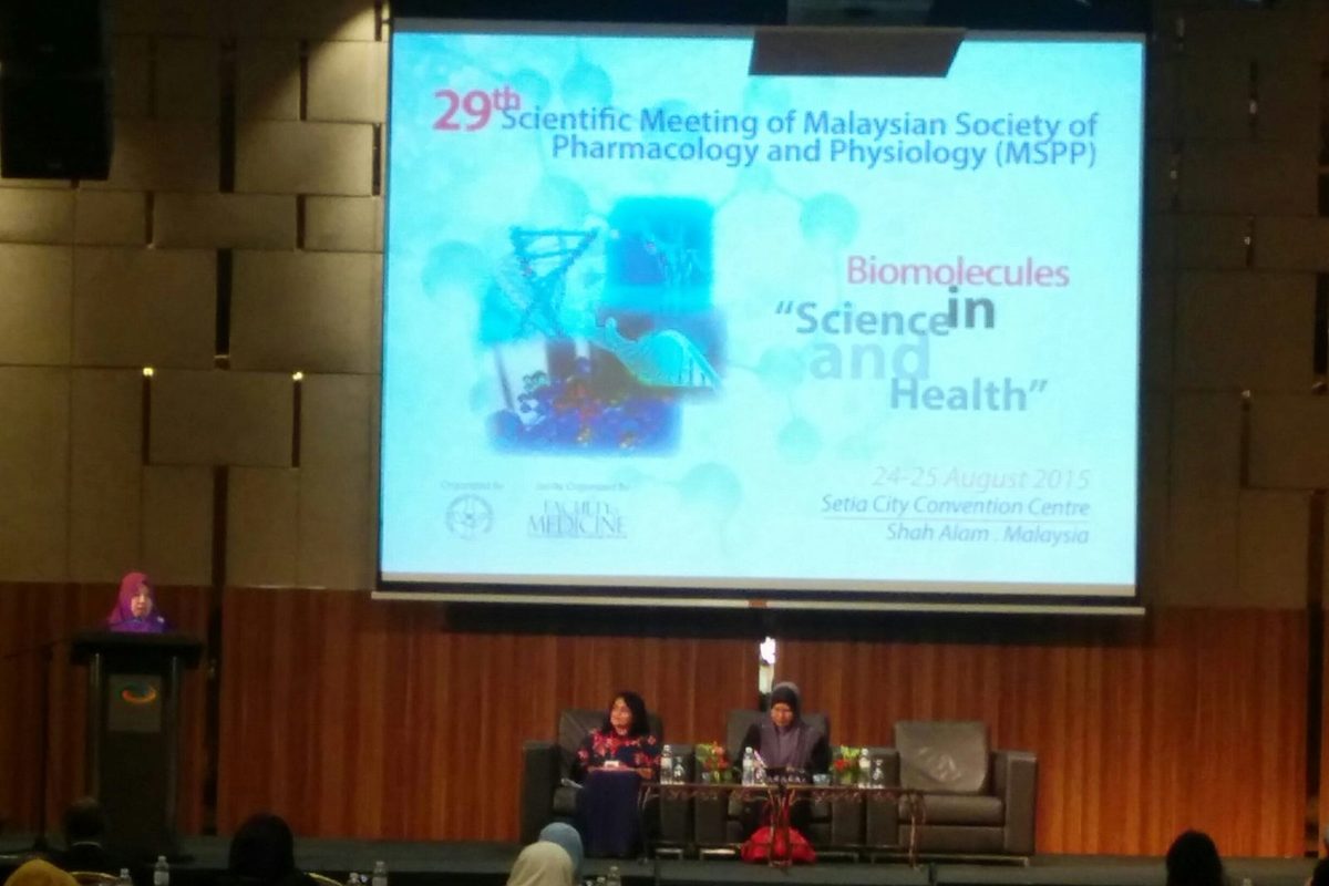 A session on stage, with the meeting's title, theme, dates and venue shown on the screen above