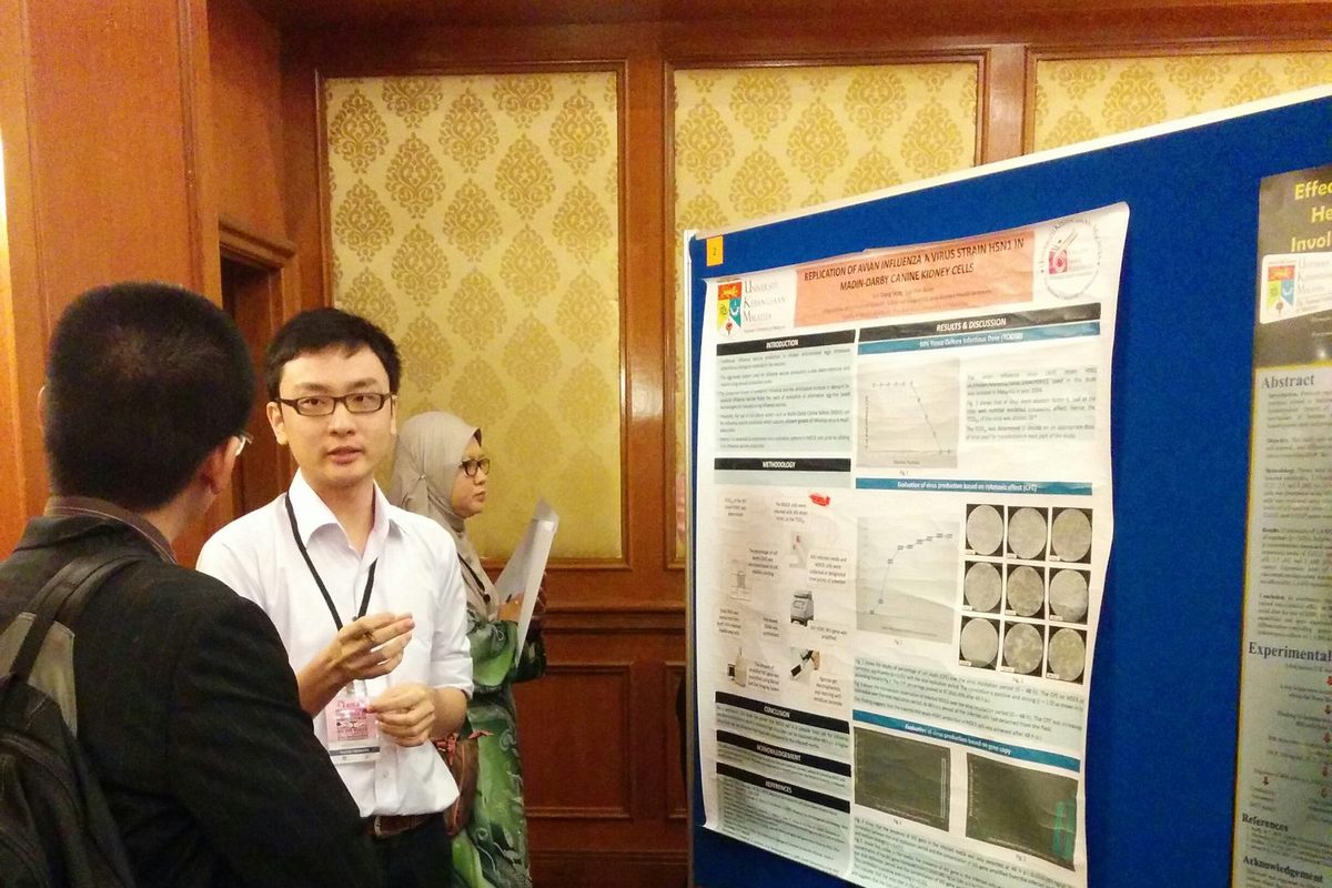 A poster presenter explains his research poster to a delegate beside a blue poster board