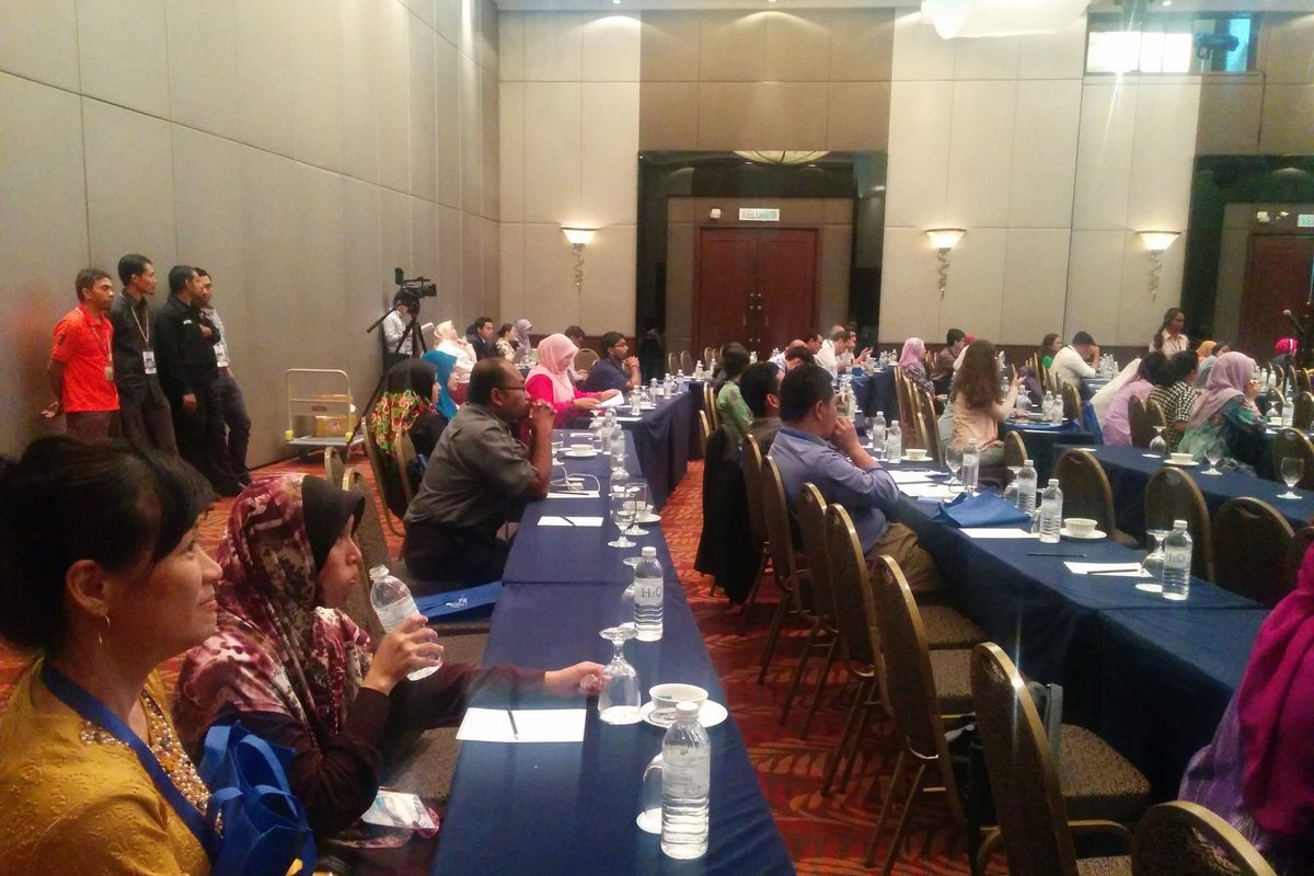 Delegates seated along rows of long tables in a hotel function room