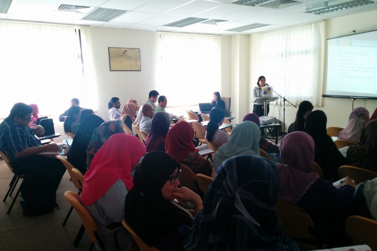 Workshop participants seated in rows in a bright seminar room, facing a speaker and a screen