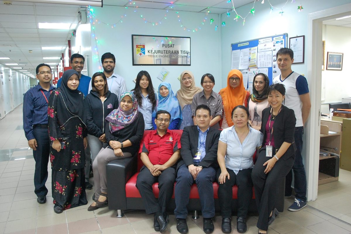 A group of seventeen people, some seated on a red sofa, under the Pusat Kejuruteraan Tisu (Tissue Engineering Centre) sign