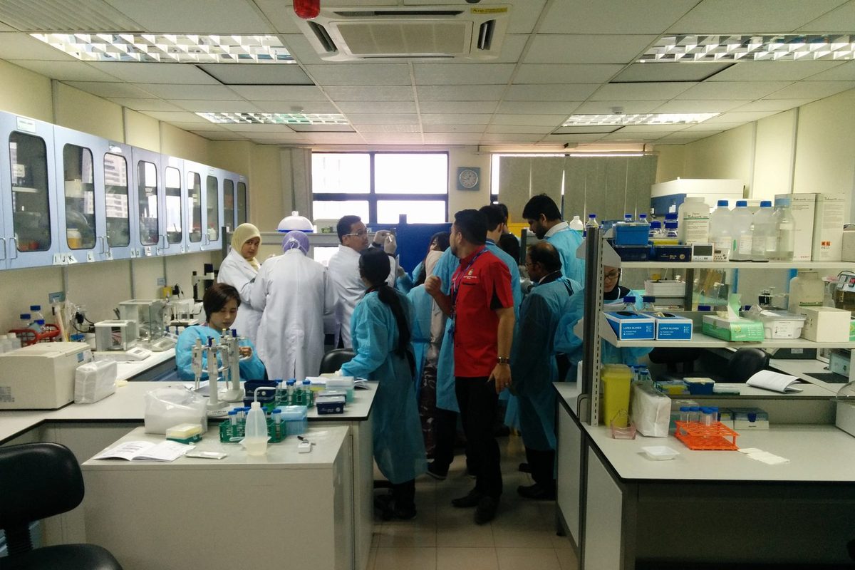 Participants in blue laboratory gowns gathered around the benches of a laboratory
