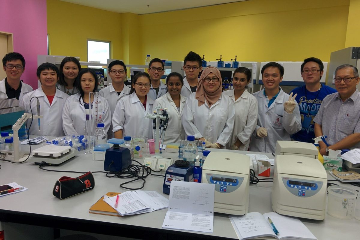 A group of participants and trainers in lab coats standing behind a laboratory bench
