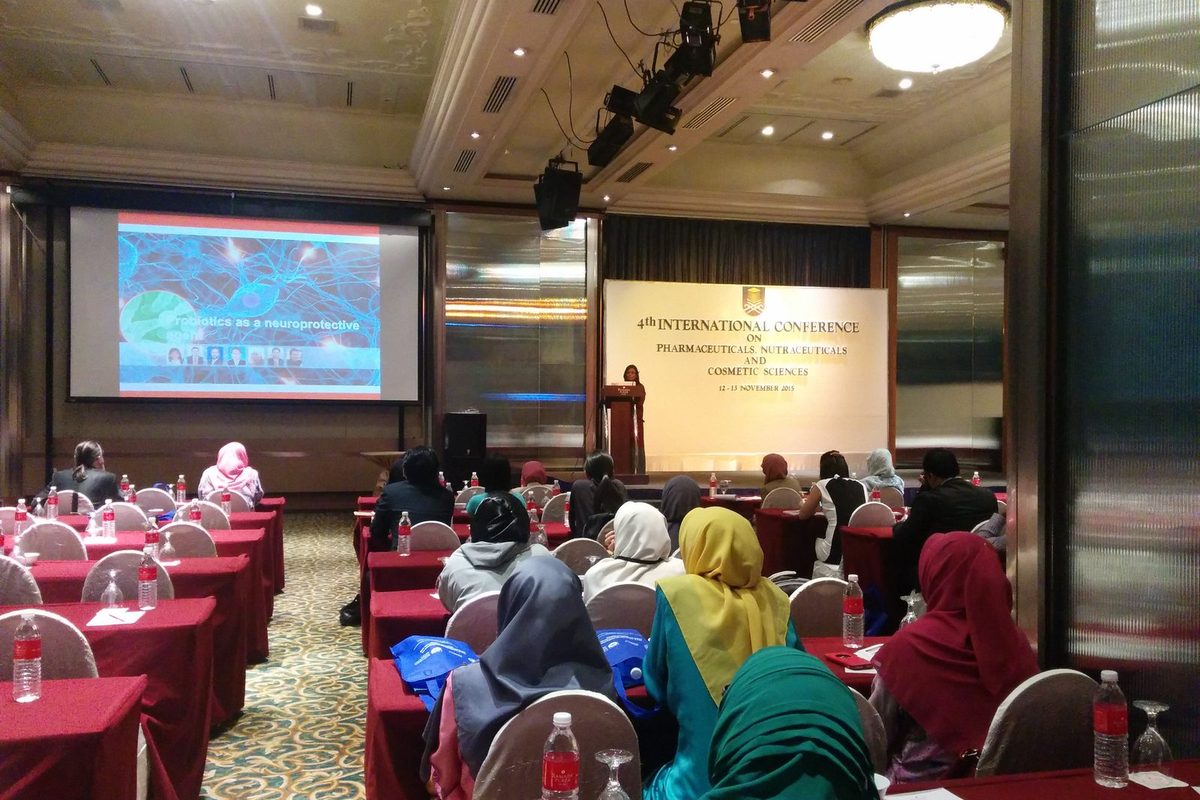 Delegates at tables covered in red cloth following a talk, with the conference banner beside the stage