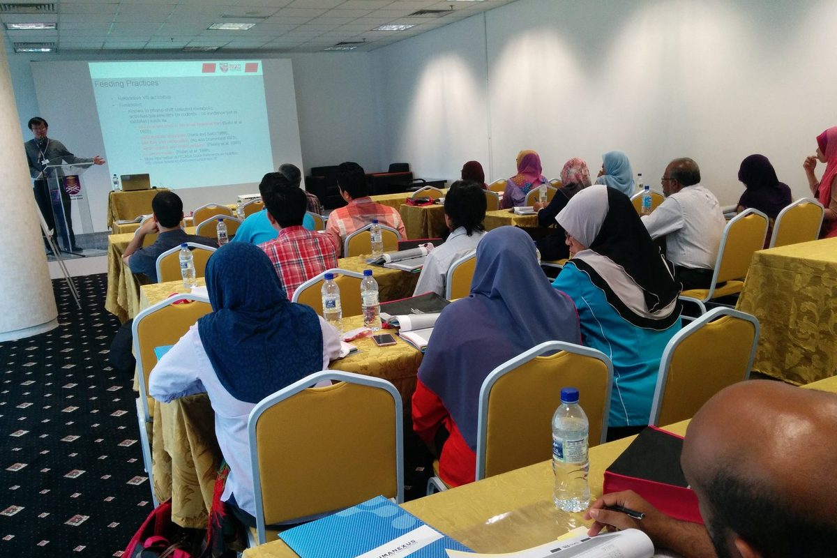 A speaker at the front of the lecture room, with participants at tables