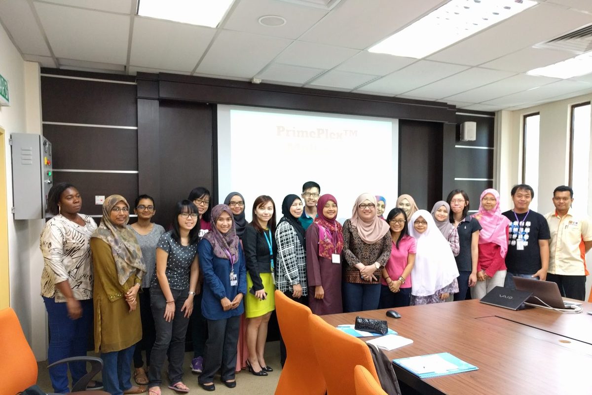 Participants and trainers stand for a group photo in the seminar room, with a title slide on the screen behind them