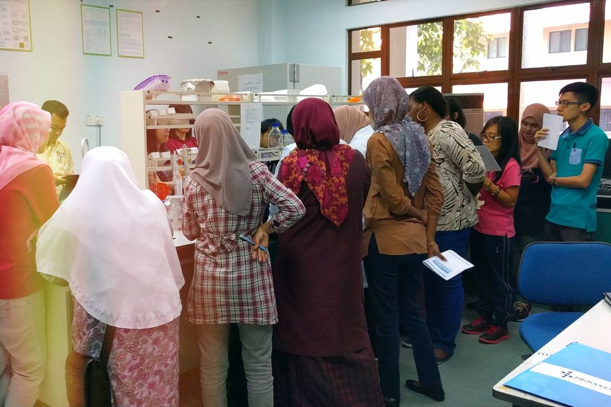 Participants gather around a laboratory bench to watch a step of the ELISA demonstration