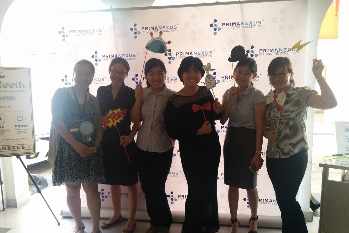 Six people holding photo props in front of the Prima Nexus logo backdrop