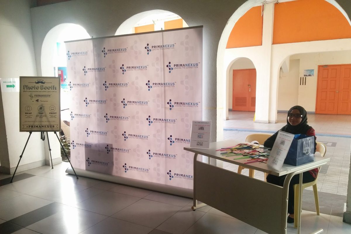 Prima Nexus photo booth: a logo backdrop, a Photo Booth sign on an easel and a props table with a person seated at it