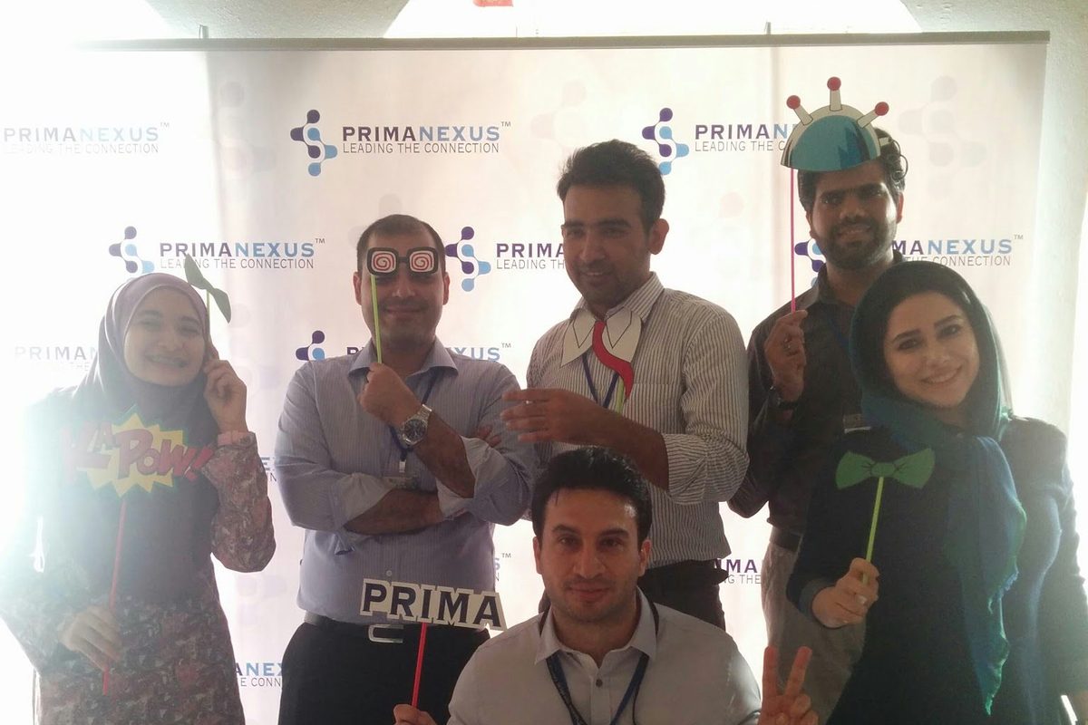 Six people posing with props, including a PRIMA sign, in front of the Prima Nexus backdrop