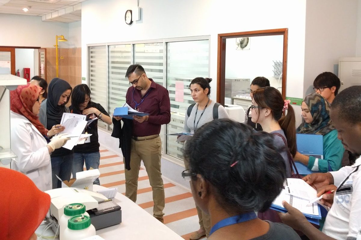 A group of participants with printed notes gathers around a laboratory bench