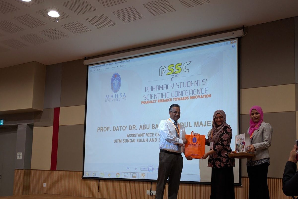 Three people on stage during a presentation in front of the conference screen.