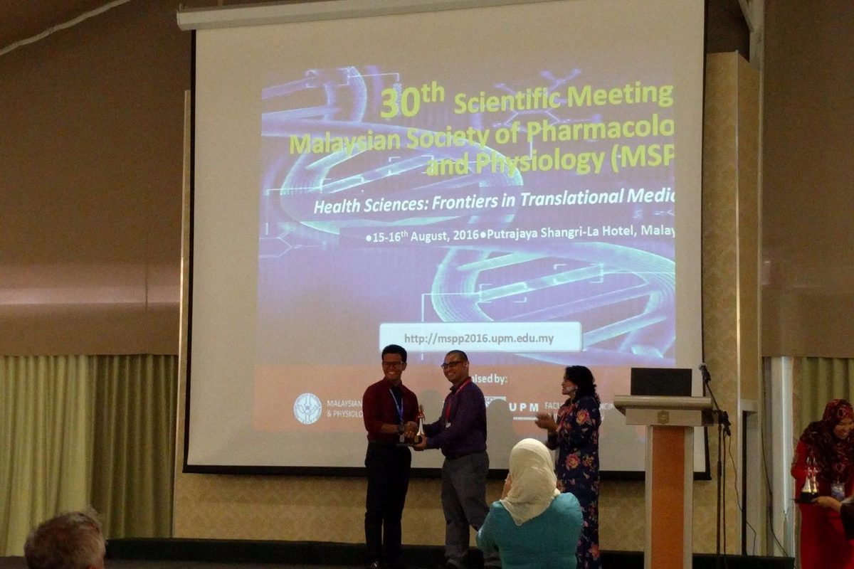 A trophy handed over on stage in front of the MSPP 2016 screen as the audience watches