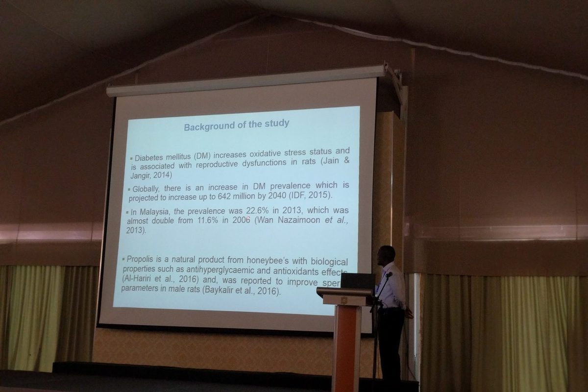 A presenter at the lectern beside a slide on diabetes and propolis in rats