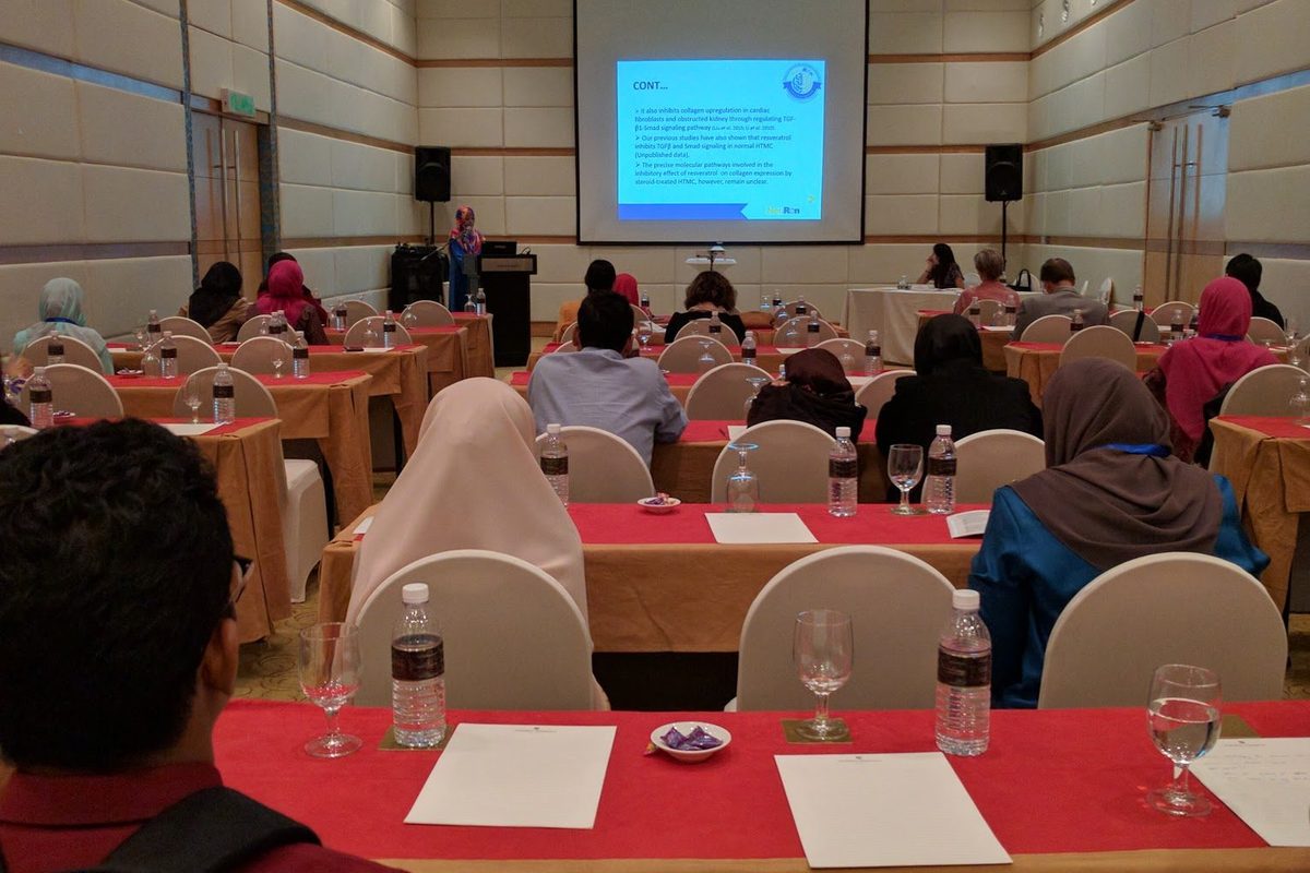 Delegates at red-covered tables listening to a talk in a hotel meeting room